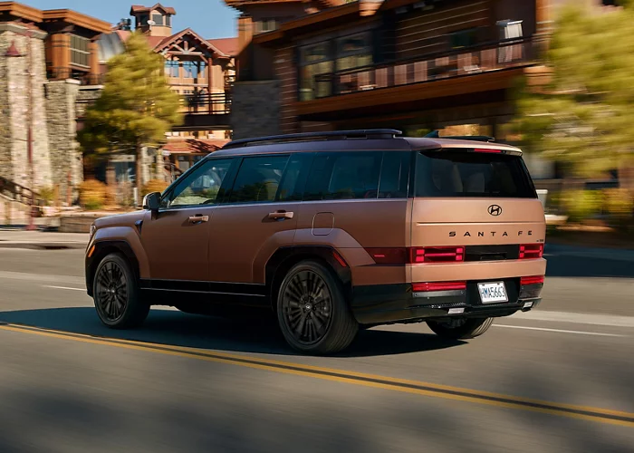 2025 Hyundai Santa Fe HEV in bronze driving through a town with rustic wooden buildings. Available now at Jerry V Honolulu Hyundai.