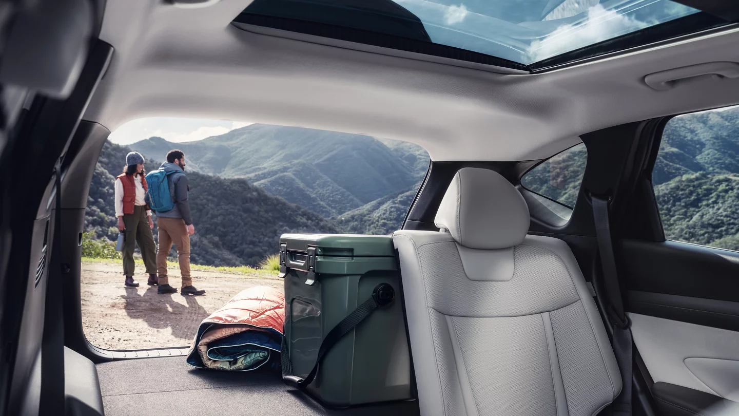 Spacious trunk of the 2025 Hyundai Tucson with light gray leather seats, a cooler, and camping gear inside, overlooking a scenic mountain view. Available now at Jerry V Honolulu Hyundai.
