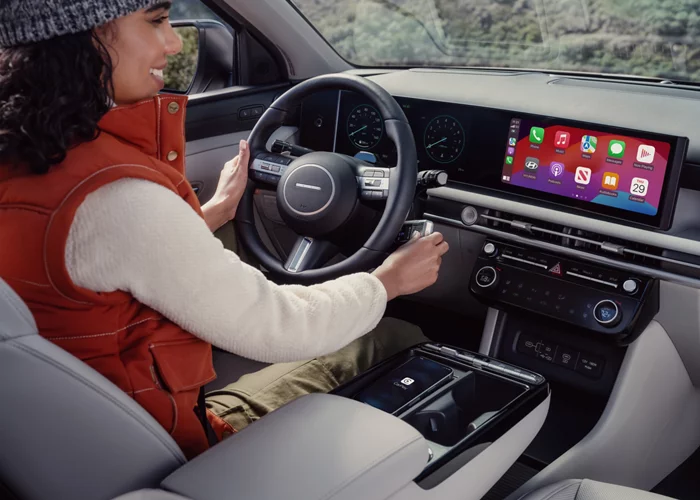 A driver sitting inside a Hyundai Tucson, displaying the sleek interior with a digital dashboard and Apple CarPlay interface.