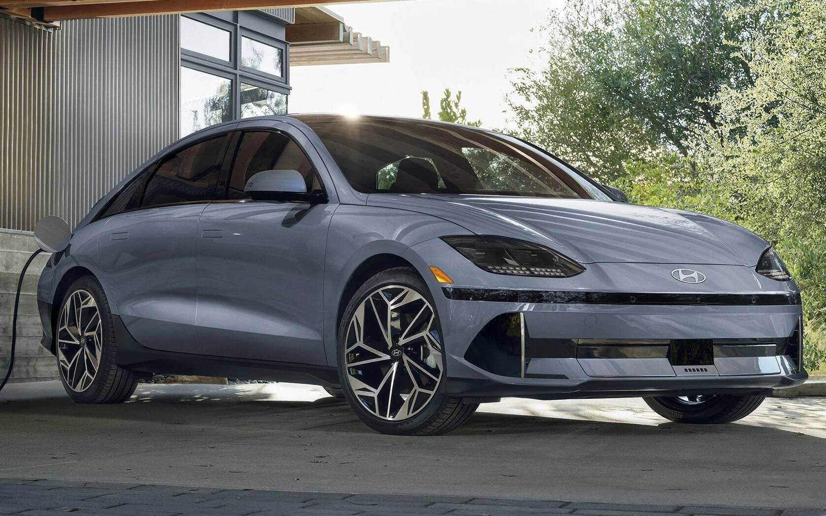2025 Hyundai Ioniq 6 in light blue charging at a home station with modern architecture and trees in the background. Available now at Jerry V Honolulu Hyundai.