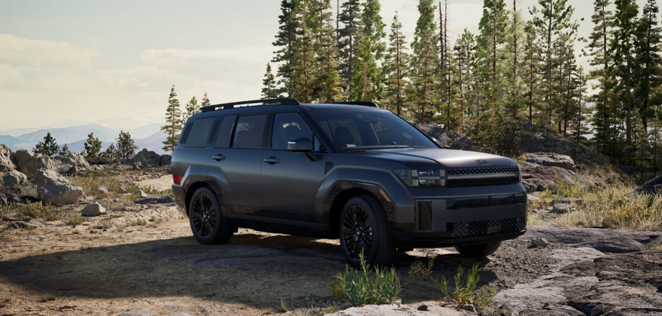 Dark gray 2026 Hyundai Sante Fe Hybrid SUV parked on a rocky trail surrounded by pine trees.