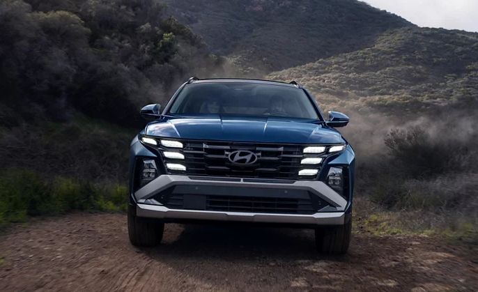 2026 Hyundai Tucson front view driving on a rugged dirt trail with mountains in the background.