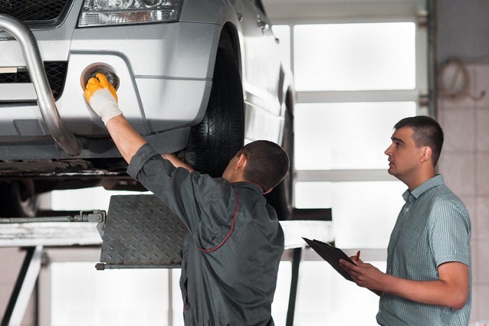 Two mechanics inspecting a car in a professional service bay at Jerry V Honolulu Hyundai.